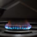 Flacără albastră de gaz la ochiul unui aragaz, într-o bucătărie slab luminată